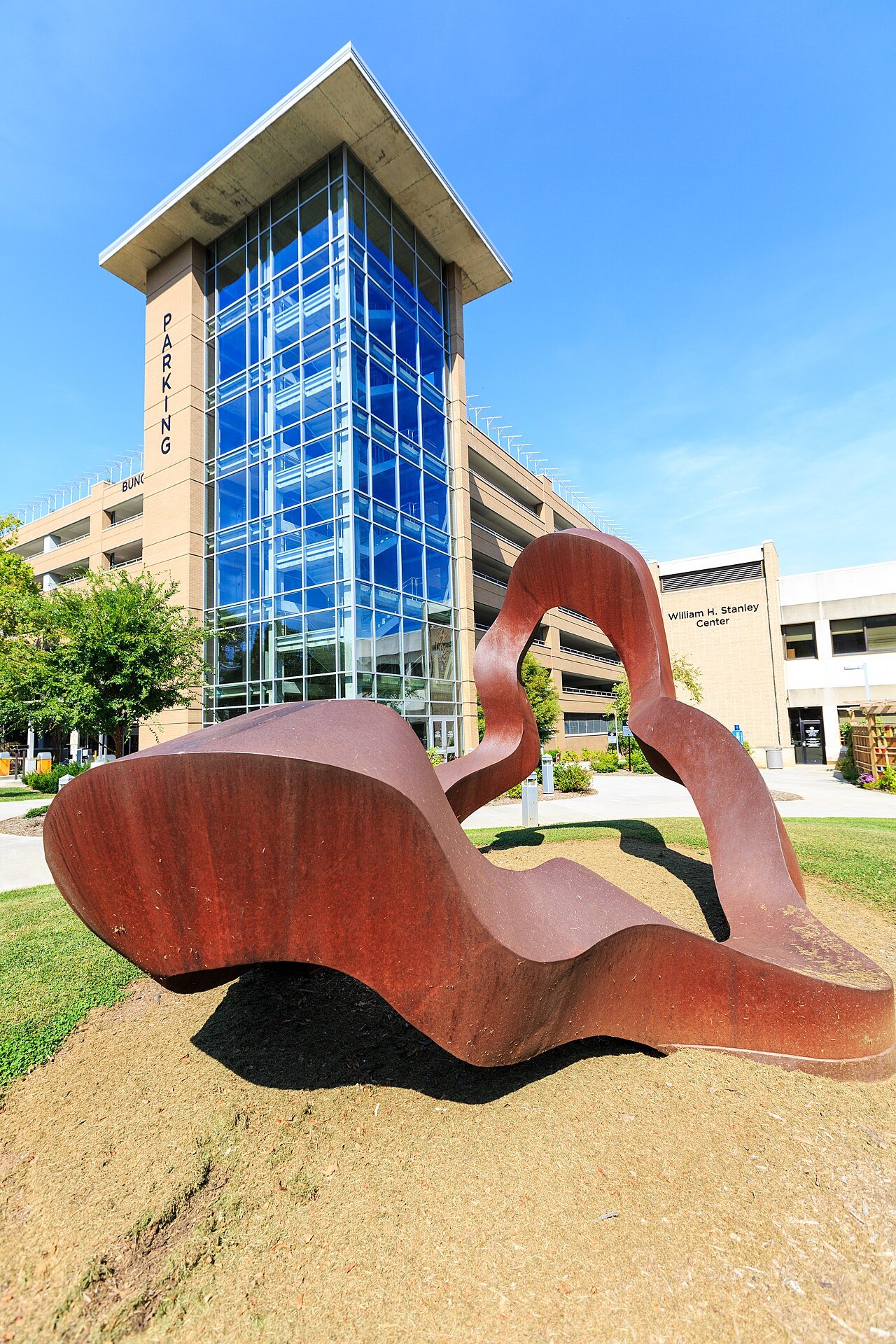 A rust-red steel sculpture in front of a glass stair tower in Asheville.