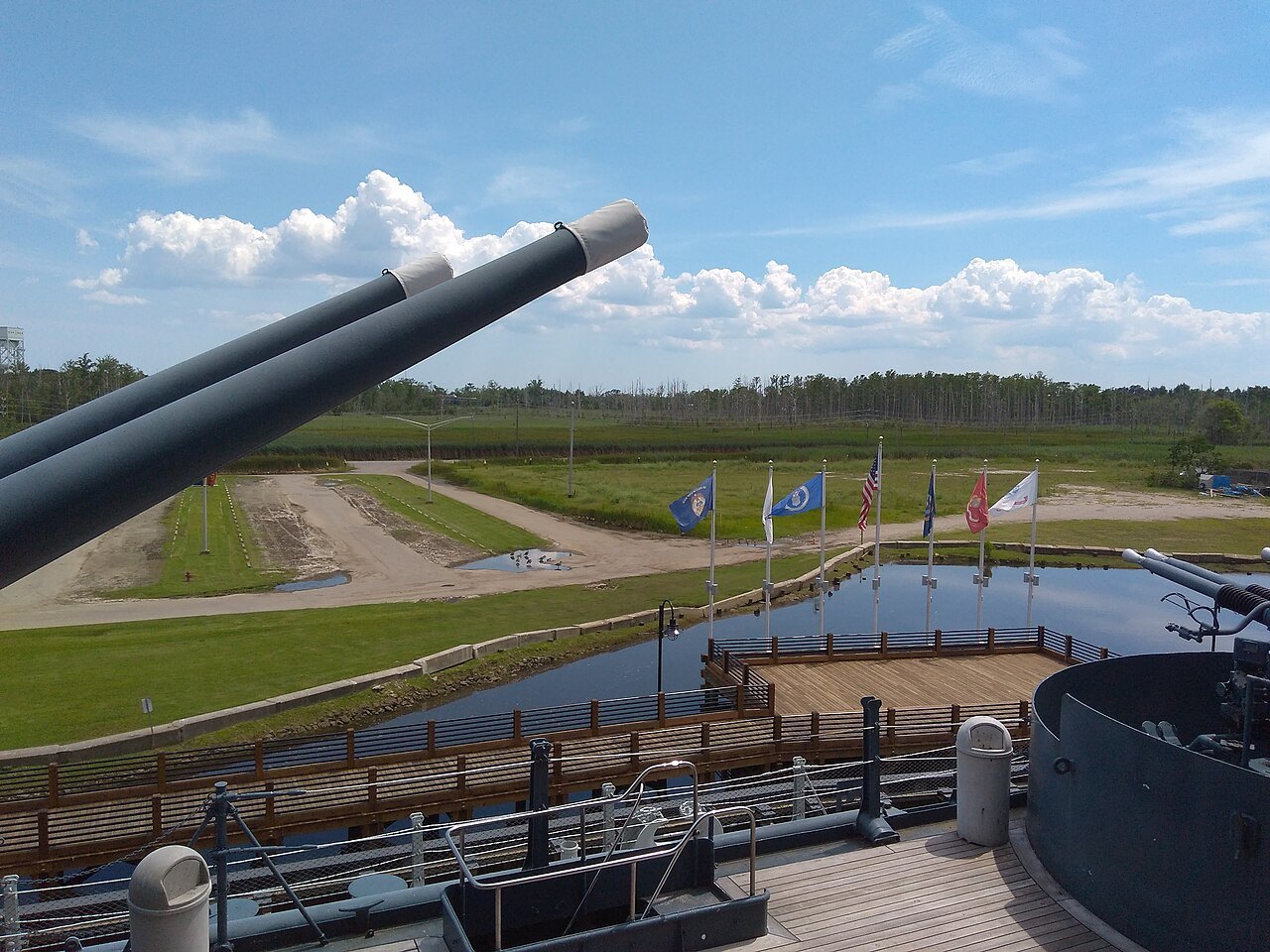 The barrels of a gun turret above the flags and grounds beside the battleship.