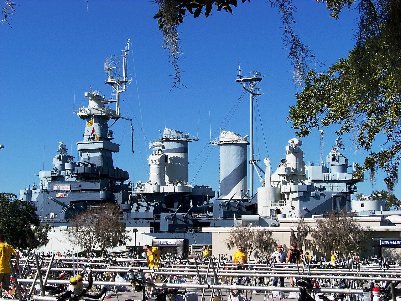 The battleship's upper decks crowded with visitors, seen from the river bank.