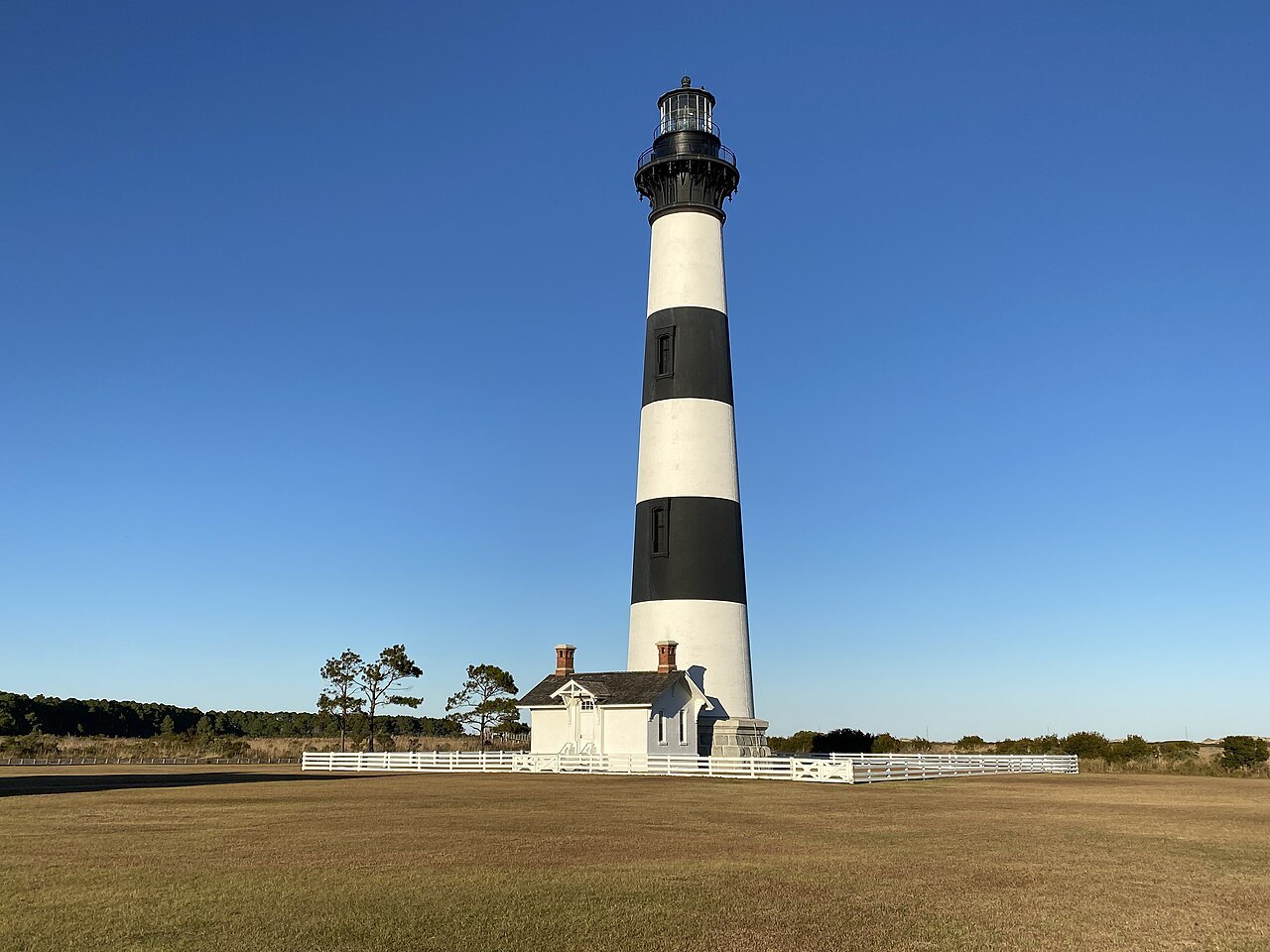 The black-and-white bands of Bodie Island Lighthouse and its keepers' house under a clear sky.