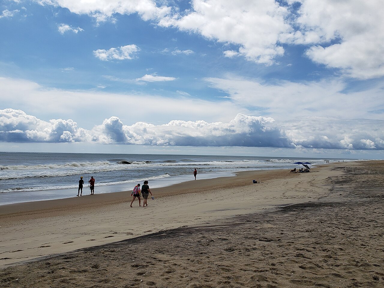 Visitors walking the beach on Hatteras Island under summer clouds.