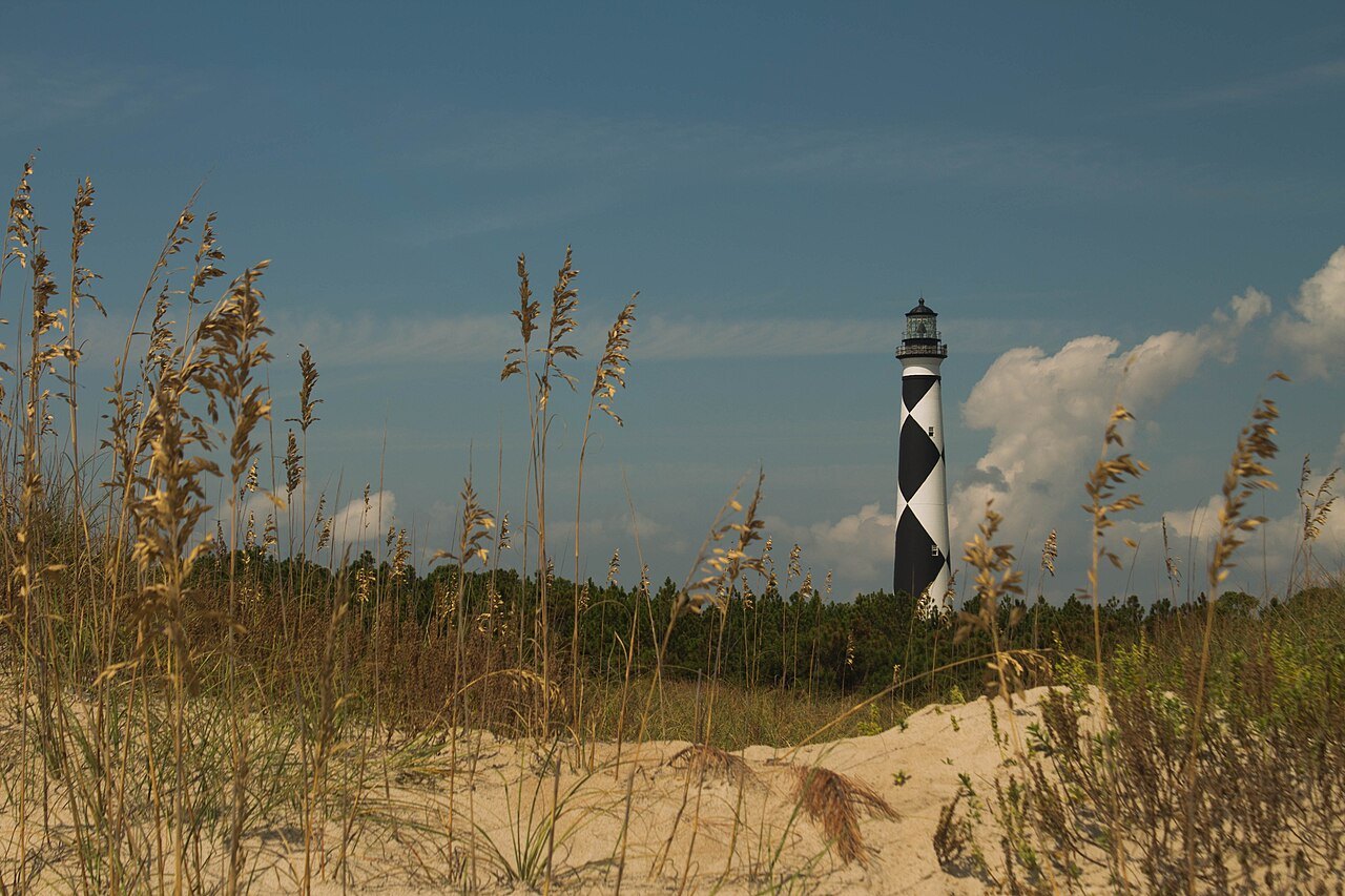 The diamond-marked lighthouse seen through sea oats from the ocean-side beach.