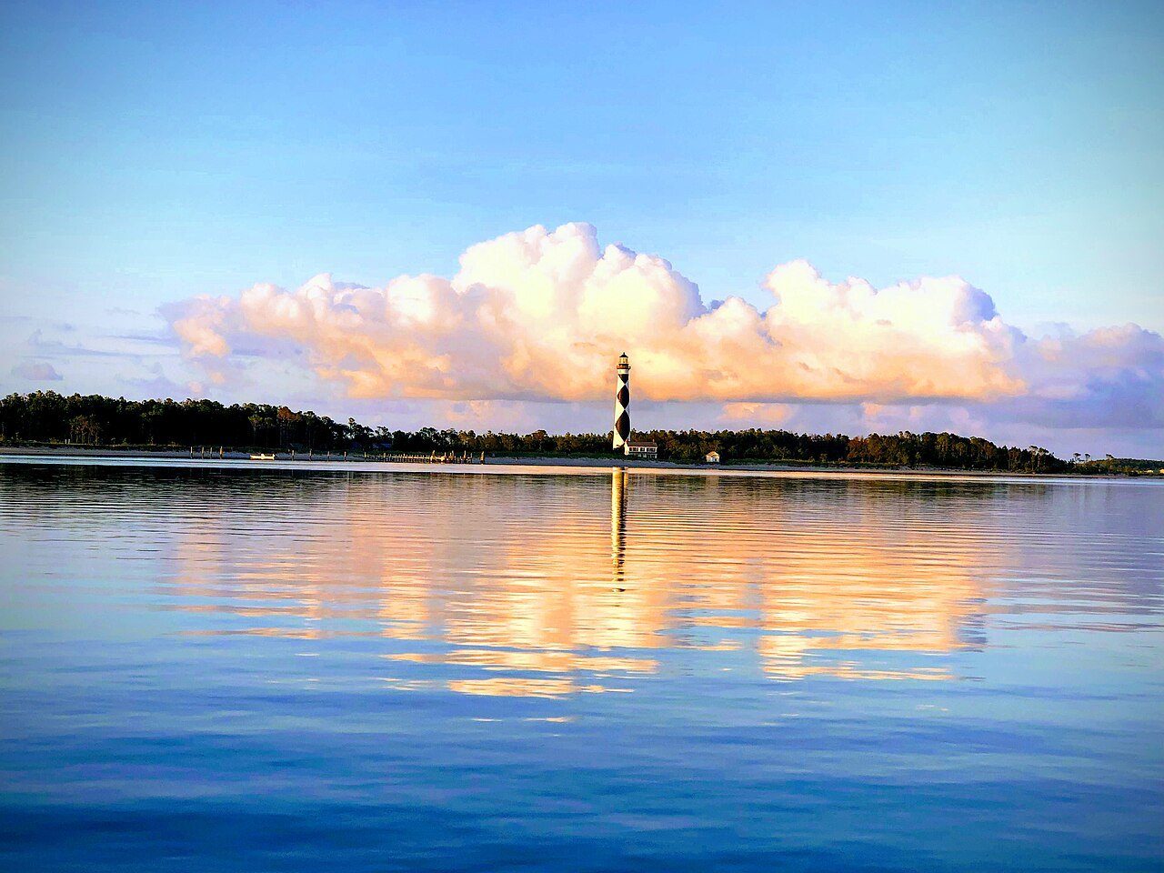 The Cape Lookout Lighthouse reflected in calm water at sunrise.