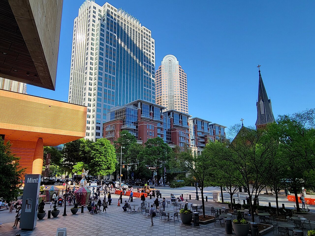 Crowds on a plaza below the Wells Fargo towers and a church spire.
