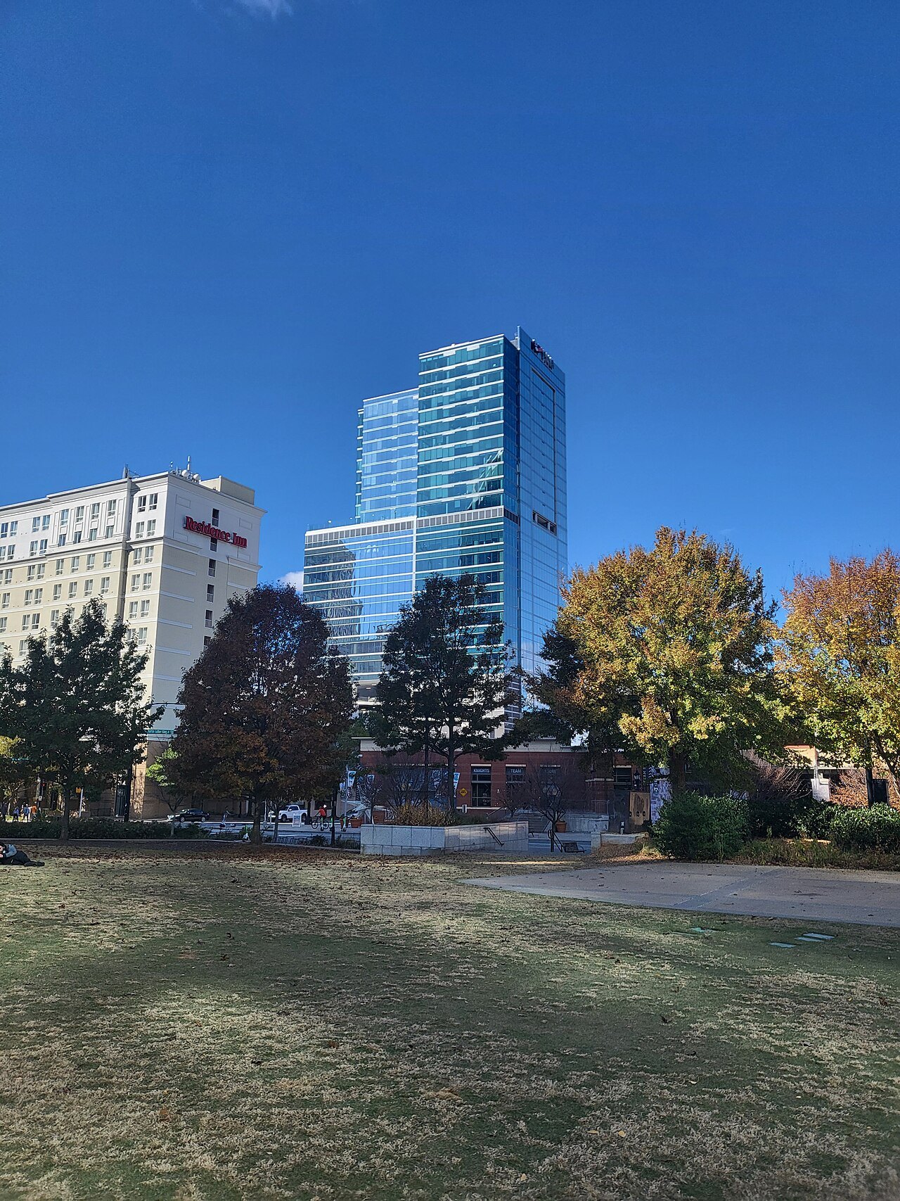 A glass office tower above autumn trees and a park lawn in Uptown.