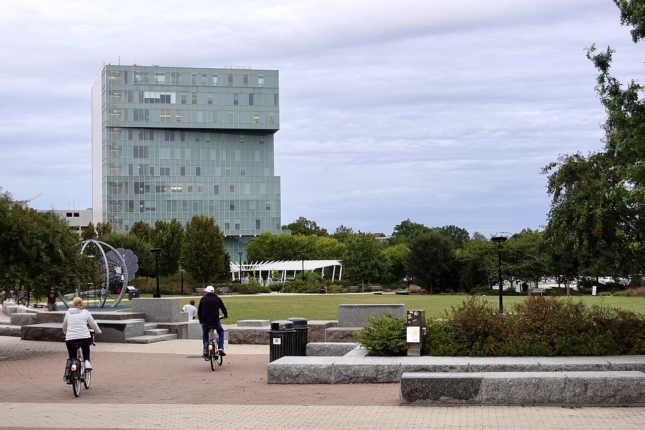 Cyclists crossing First Ward Park below a modern office tower.