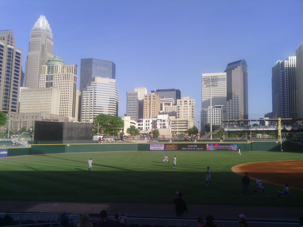 Uptown towers rising beyond the field of the downtown ballpark during a game.