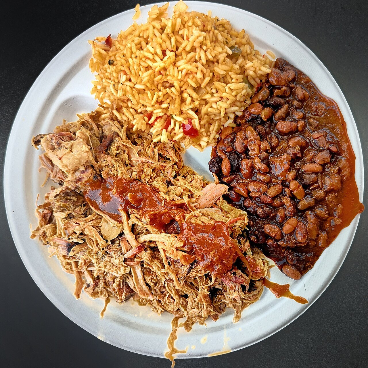 A plate of North Carolina pulled pork with rice and baked beans.