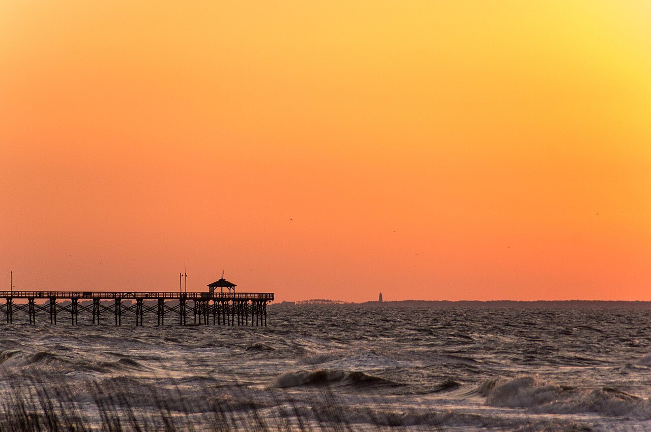 A fishing pier silhouetted against an orange dawn on Oak Island.