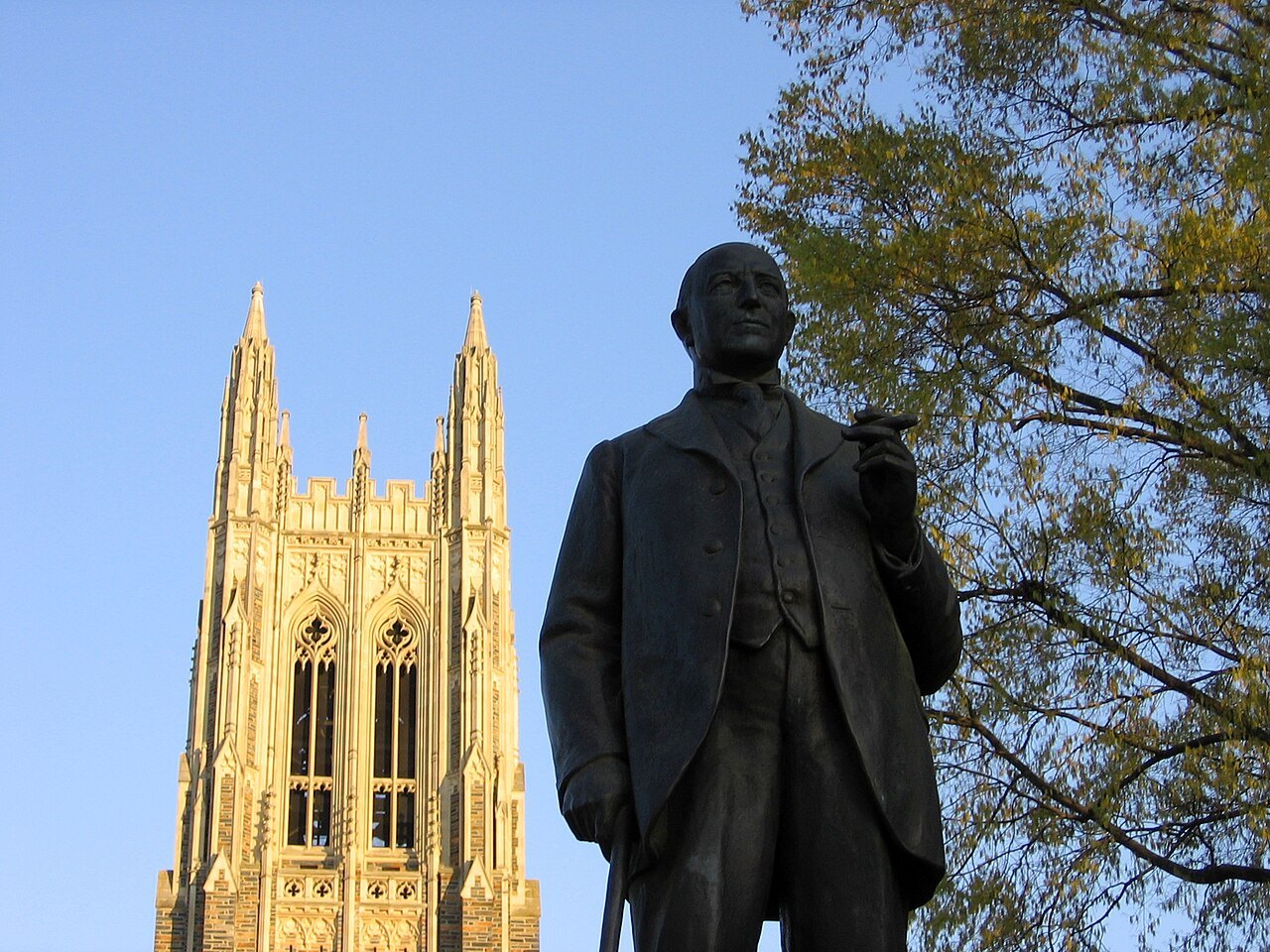 A statue of James B. Duke before the golden stone towers of Duke Chapel.