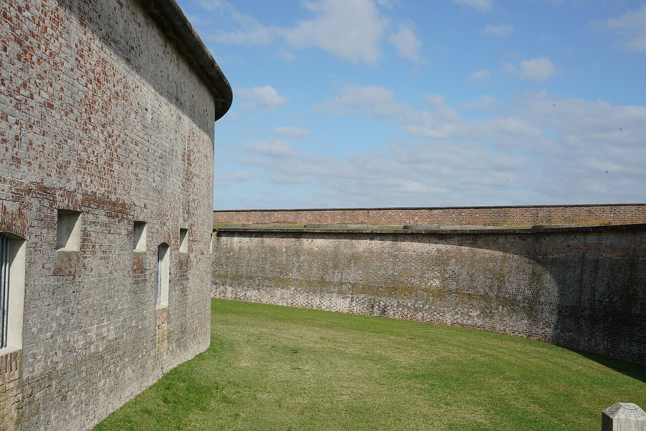 The curving outer wall of Fort Macon above the grass of its ditch.