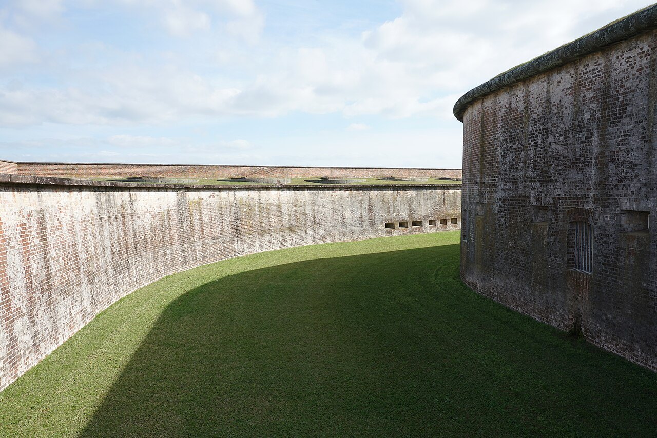 The curving brick wall of Fort Macon above its grassy ditch.