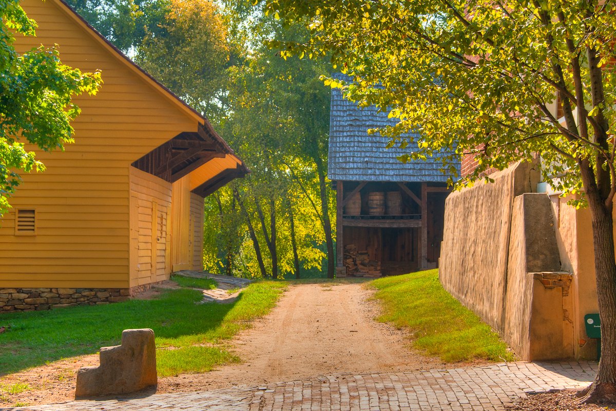 A dirt lane between an ochre building and a timber shed in Old Salem.