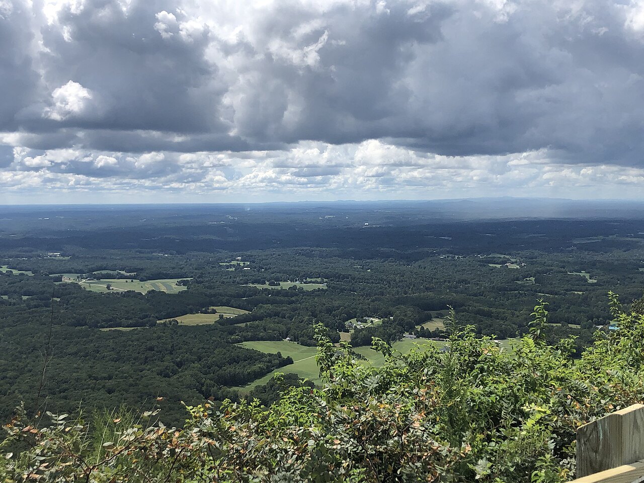 Farmland spreading to the horizon below Pilot Mountain under big clouds.