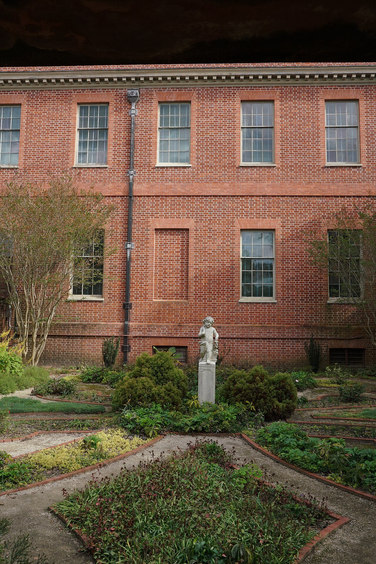A garden statue below the brick wing of Tryon Palace.
